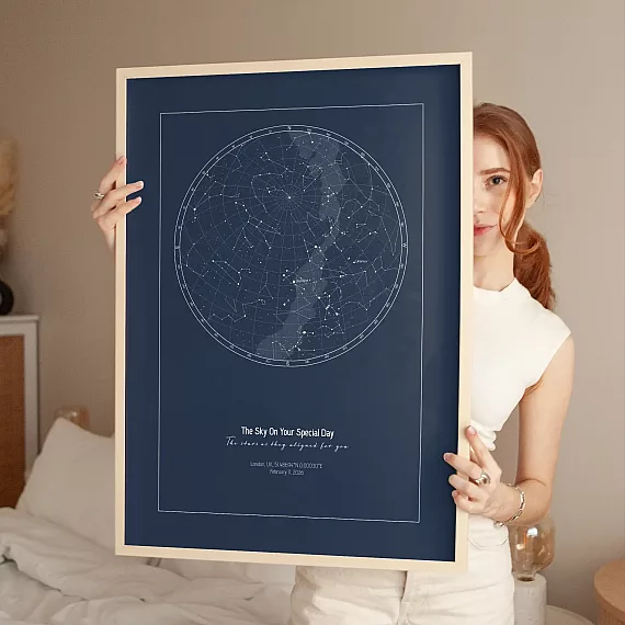Dark blue Birthday Star Map poster held by woman in bedroom.