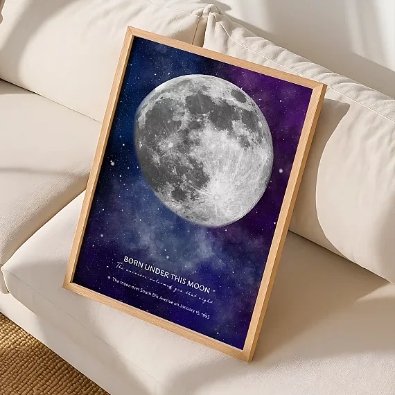 Framed birthday moon poster with a glowing full moon displayed on a cream sofa.