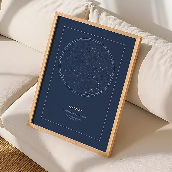 Framed custom star map print with a navy night sky design displayed on a cream sofa in a cozy home setting