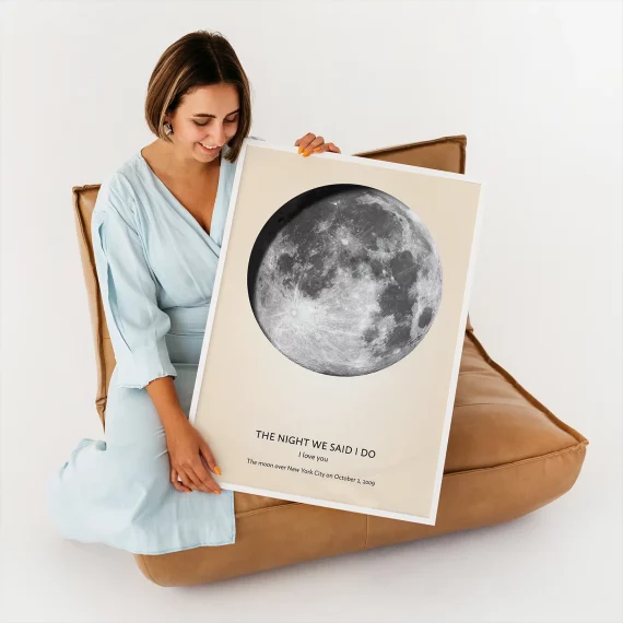 Woman holding personalized moon phase poster showing the moon on a special date with custom text.