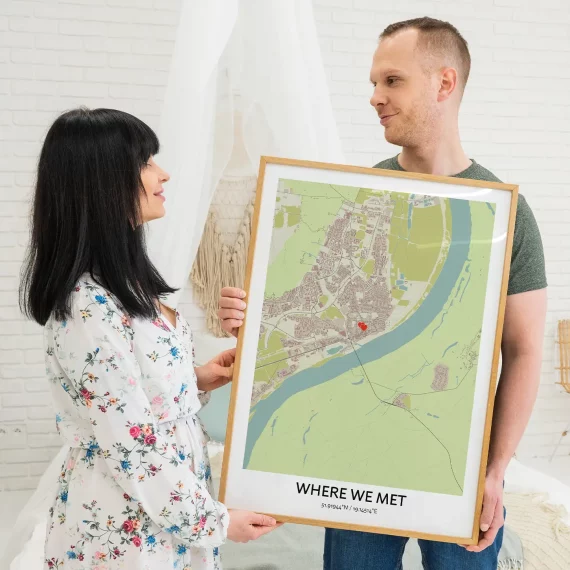 Couple holding a framed “Where We Met” map poster with a marked location and coordinates.