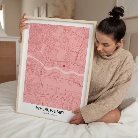 Woman holding a personalized “Where We Met” map poster in a soft pink color theme with a heart marker.