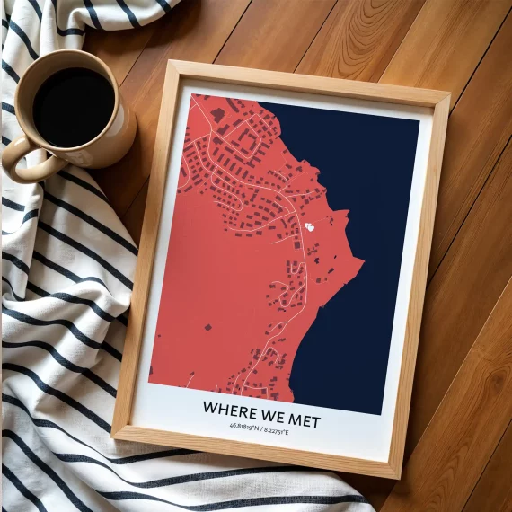 Modern “Where We Met” map poster in bold colors placed on a wooden floor next to a coffee cup.