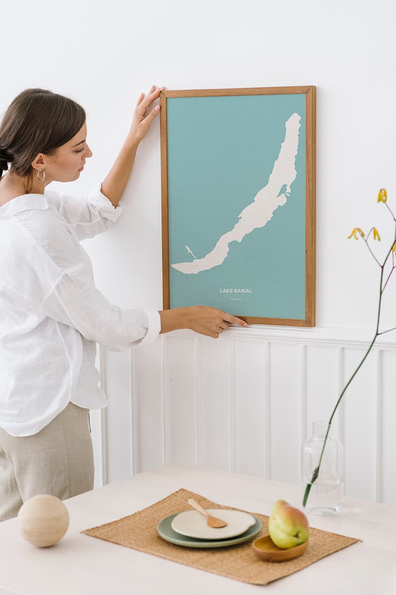 Woman decorating wall with lake topography art with Lake Baikal shape.