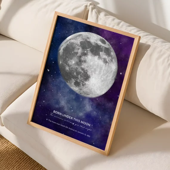 Framed birthday moon poster with a glowing full moon displayed on a cream sofa.