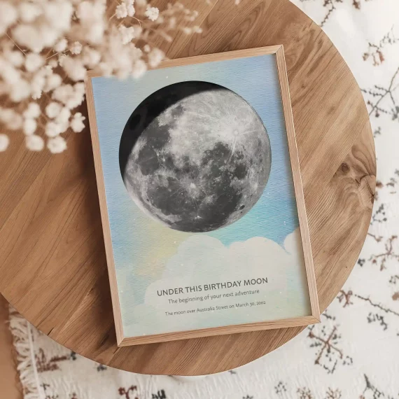 Watercolor birthday moon poster displayed on a round wooden table with dried flowers.