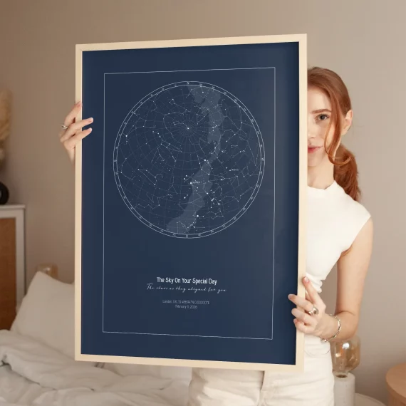 Dark blue Birthday Star Map poster held by woman in bedroom.
