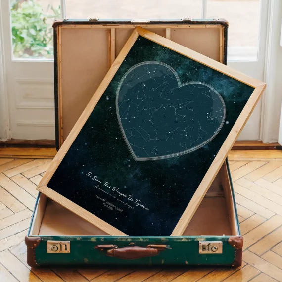 Heart-shaped Stars The Night We Met poster in a wooden frame displayed inside an open vintage suitcase on a wooden floor.