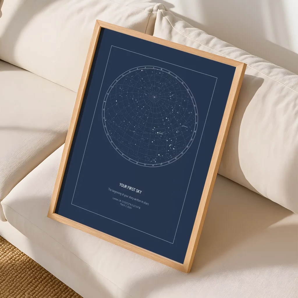 Framed custom star map print with a navy night sky design displayed on a cream sofa in a cozy home setting