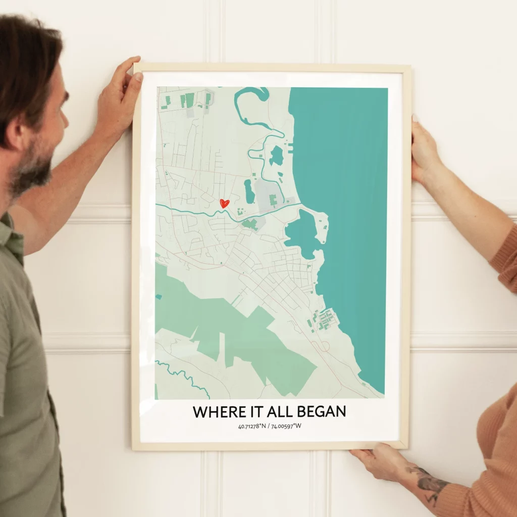 Couple placing a Where It All Began custom map poster on the wall with a marked location.