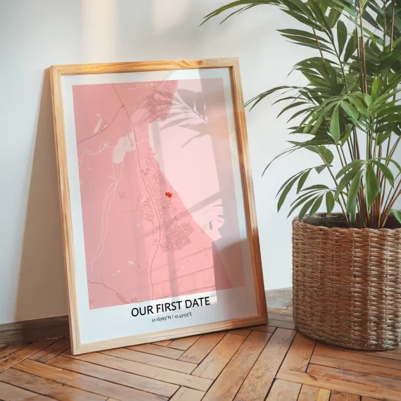Our First Date Map poster in pink tones displayed on the floor next to a plant in a cozy home setting.
