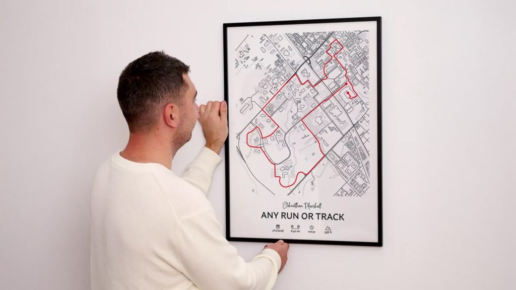 Runner hanging a custom route map poster featuring a recorded running track route and performance statistics, creating a meaningful keepsake for runners.