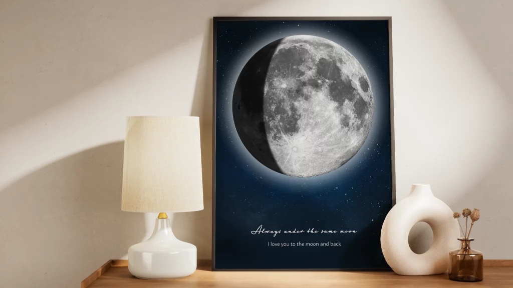Personalized waning moon print in a black frame with a glowing moon phase, starry night background, and custom message on a wooden shelf.