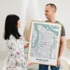 Couple holding a framed Where We Met map print with a red heart marker