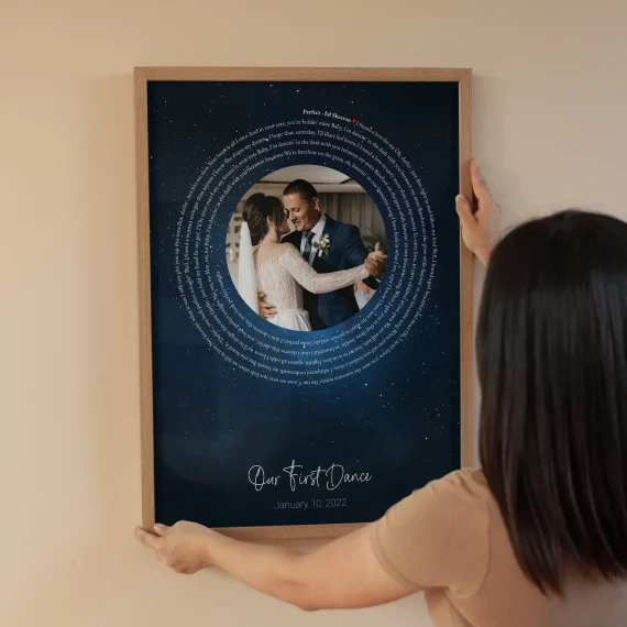 Person hanging First Dance Song Lyrics with Photo poster with a wedding photo and circular lyrics on the wall.