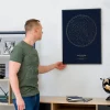 Man looking at a framed personalized company founding star map with gold details on a navy background.